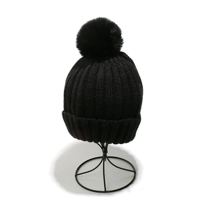 Detail of black knit beanie with soft pompom and classic ribbed texture for winter