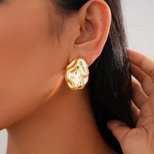 Detailed close-up of large irregular molten texture gold stud earrings on a female model
