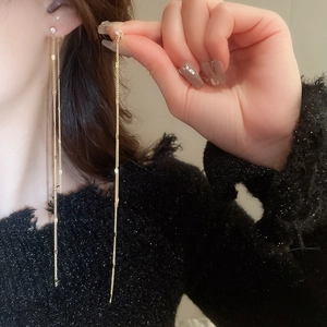 Close-up of gold tassel earrings with zircon studs worn by a model on black knit