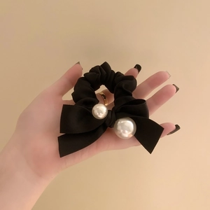 Elegant black velvet bow hair scrunchie with large pearls and satin finish on model's hand