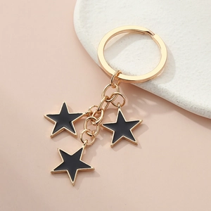 Detail of gold-plated alloy star keychain with black enamel drips on a soft pink background
