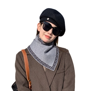 Gray knitted scarf with black Greek key pattern worn by a model in stylish winter attire