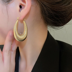 Detail of large gold hoop earring with spiral texture shown on model in warm lighting