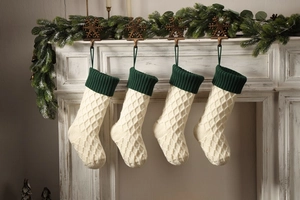 Nahaufnahme von beige gestrickten Weihnachtssocken mit grünen Bündchen an einem Kamin