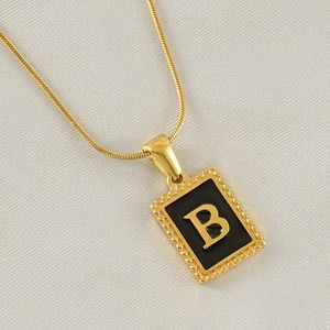 Detail of a rectangular gold letter B pendant with black inlay on a fine snake chain necklace