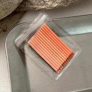 Detail of matte orange hairpins neatly arranged in a clear pouch on a metal tray