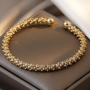 Macro shot of gold geometric open bangle with spiral texture and metal balls detail