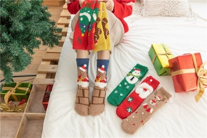 Close-up of thick coral fleece Christmas socks with festive patterns on a cozy white bed