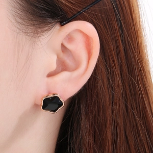Close-up of a black four-leaf clover earring with gold trim worn by a model