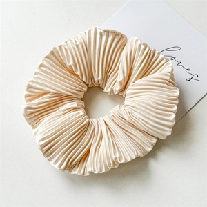 Macro shot of cream-colored pleated satin scrunchie with detailed accordion fold texture
