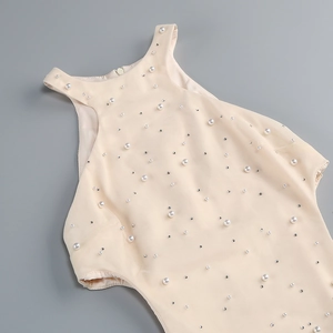 Close-up of beige halter dress featuring dense white pearls and sparkling rhinestones