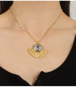 Detailed view of an elegant gold necklace featuring a square glass stone and fan pendant