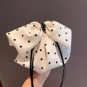 Polka dot bow hair clip with black beads shown on a minimalist grey background