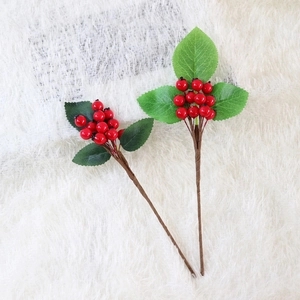 Artificial red holly berry stems with green leaves on white plush background for Christmas