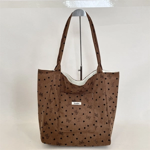 Detail of brown corduroy tote bag featuring heart and bow patterns with a front pocket
