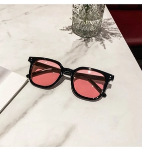 Close-up of black square sunglasses with pink lenses and silver dot details on marble