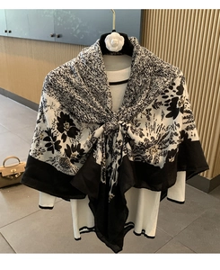 Detail of floral linen blend scarf in black and beige draped over a white sweater