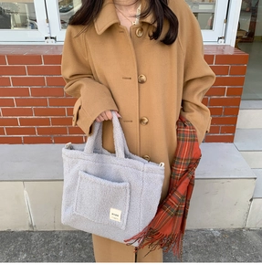 Close-up of gray faux shearling tote bag with BYBR label held by model in autumn outfit
