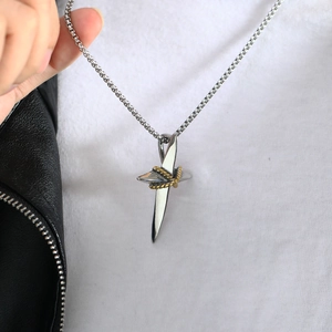 Close-up of silver cross pendant with golden rope wrap detail held in hand