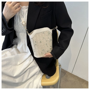 Gros plan du sac seau en paille crème avec broderie florale verte sur mannequin