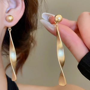 Gros plan de boucles d'oreilles spirales torsadées dorées mates au design élégant