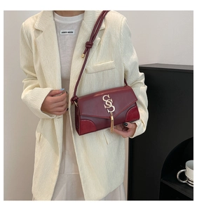 Detail of burgundy flap shoulder bag featuring a gold logo and tassel on elegant suit