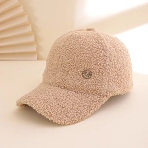 Detail of beige sherpa baseball cap featuring a circular metallic M logo and soft teddy fur