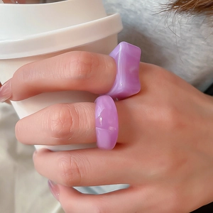 Detail of purple acrylic rings with translucent finish on hand holding a white coffee cup