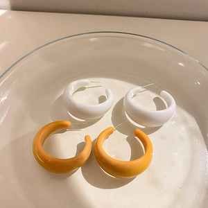 Macro detail of thick C-shaped hoop earrings in white and ginger yellow finishes