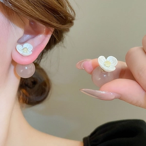 Elegant floral resin ball earrings in light gold finish worn on a warm grey background