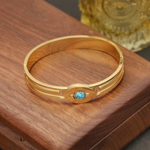 Gold evil eye bangle with blue turquoise center on dark wooden jewelry display box