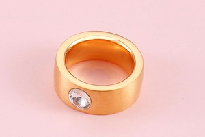 Detailed top view of gold wide band ring with a round zircon and brushed metal finish