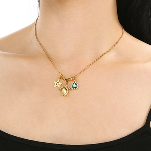 Close-up of gold necklace with star, turtle and green gemstone pendants on model