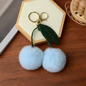Detail of light blue faux fur cherry keychain with green leather leaves and gold hardware