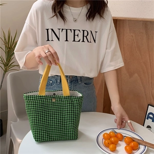 Detailed view of a green houndstooth wool tote bag with yellow handles held by a model