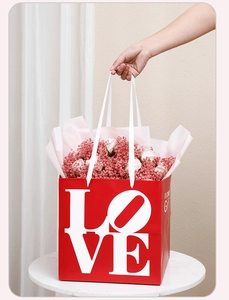 Close-up of a red LOVE themed gift bag with a bouquet of pink and white flowers