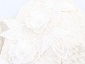 Détail de fleurs en dentelle 3D et perles artificielles sur tissu brodé blanc