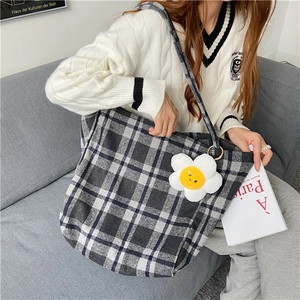 Detail view of plaid wool tote bag with white flower charm and sweater outfit