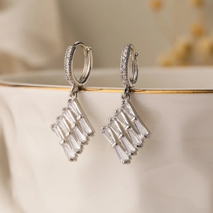Silver geometric earrings with emerald-cut zircon hanging on a white porcelain bowl