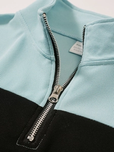 Détail du col zippé pour homme montrant la texture gaufrée bleue et l'étiquette