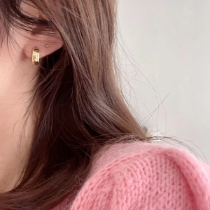 Close-up of polished gold hoop earrings worn by a model in a pink knit sweater