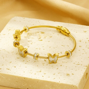 Detail of a gold twisted wire bracelet with butterfly charms on a stone pedestal