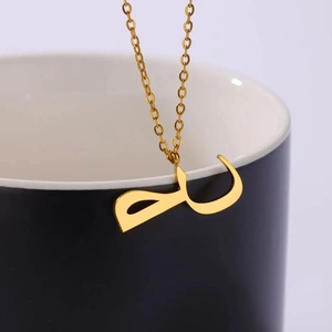 Golden stainless steel Arabic script pendant necklace hung on a modern ceramic cup
