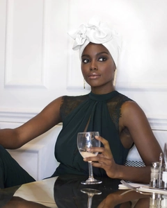 Detail eines weißen Turban-Hutes und eines Spitzenoberteils an einem eleganten Modell