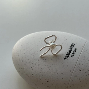 Macro detail of silver bow pearl stud earrings on a textured minimalist display