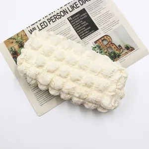 Creamy white bubble textured pencil case and makeup bag on newspaper background
