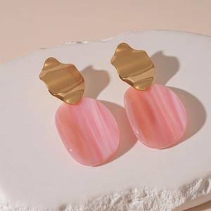 Détail de boucles d'oreilles en acrylique rose avec pièces dorées sur socle en pierre