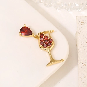 Pendentif verre à vin doré avec zircons rouges sur fond décoratif de pierres blanches