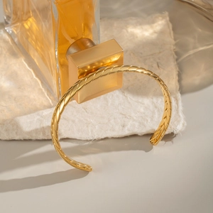 Dettaglio macro del bracciale rigido a treccia placcato oro 18K su carta bianca