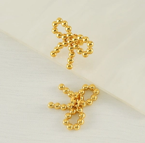 Macro detail of 18K gold bow stud earrings featuring textured beaded surface and secure backings